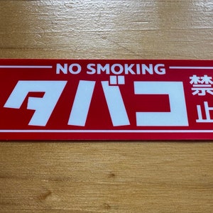May include: A red rectangular sign with white text that says "NO SMOKING" and "禁煙" in Japanese. The sign is on a wooden surface.
