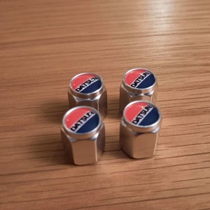 May include: Four silver tire valve stem caps with a red and blue Datsun logo.