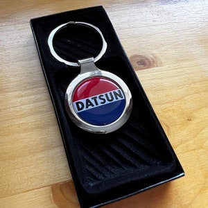 Peut inclure: Un porte-clés Datsun argenté avec un logo rouge, blanc et bleu. Le porte-clés est dans une boîte noire avec une doublure en velours.