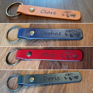 May include: Four leather keychains with metal rings. Each keychain has a different color: orange, blue, red, and green. Each keychain has a name engraved on it: Clare, Daphne, Meg, and Doris. Each keychain also has a small car image engraved on it.