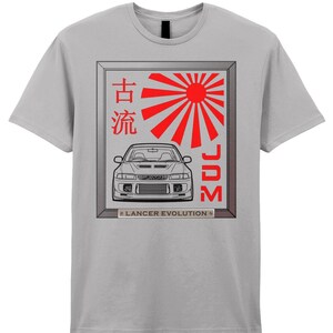 Könnte beinhalten: Hellgraues T-Shirt mit einem gerahmten Grafikdesign. Das Design zeigt eine rote aufgehende Sonne und eine Autoillustration. Der Rahmen enthält japanische Schriftzeichen und den Text "JDM". Unter dem Rahmen steht der Text "Lancer Evolution".