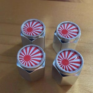 May include: Four silver-colored metal objects with a red and white sunburst design on top. The objects have a hexagonal base and a circular top with the graphic. The objects are arranged on a wooden surface.