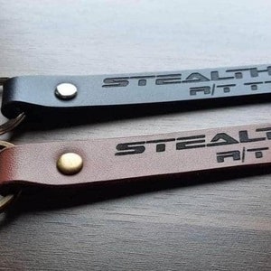 May include: Two leather keychains with metal rings. Both keychains are brown and black and have the word "STEALTH" and "R/T" engraved on them.