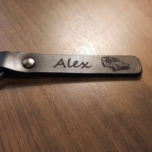 May include: A black leather keychain with a silver key ring. The keychain has the name "Alex" and a small car design engraved on it.