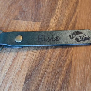 May include: A green leather keychain with a silver metal ring. The keychain has the name "Elsie" engraved on it, along with a small image of a vintage pickup truck.