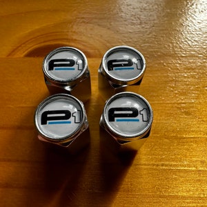 May include: Four silver tire valve stem caps with a white background and black "P1" logo with a blue stripe.