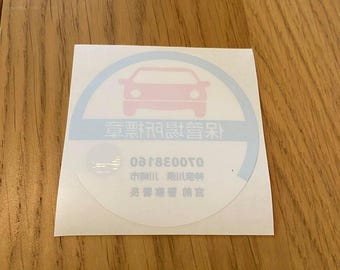 Könnte beinhalten: Ein weißer Aufkleber mit einem blauen Kreis, der eine rosafarbene Silhouette eines Autos enthält. Der Text "車両用登録済" ist in Schwarz innerhalb des Kreises. Der Text "070038160" ist in Schwarz unterhalb des Kreises. Der Text "市制施行" ist in Schwarz unterhalb der Nummer. Der Text "愛知県豊田市" ist in Schwarz unterhalb des Textes "市制施行".