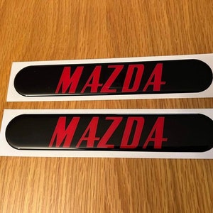 May include: Two black and white stickers with the word "MAZDA" in red lettering.