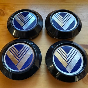 May include: Four black wheel covers with a blue and gold geometric design. The design features a stylised V shape with three horizontal lines.