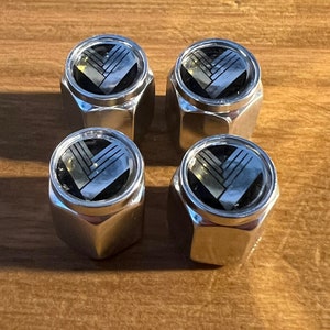 May include: Four silver chrome wheel center caps with a black and gold logo. The logo is a stylized letter V.