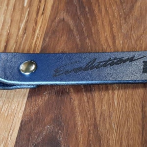 May include: A blue leather keychain with a silver ring and a black engraved inscription that reads "Evolution VIII".
