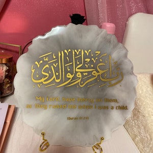 May include: A white resin plaque with a gold Arabic calligraphy design and the text "My Lord, have mercy on them, as they raised me when I was a child. (Quran 87:74)"