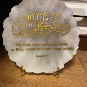 May include: A white circular resin plaque with a gold Arabic inscription and the text "My Lord, have mercy on them, as they raised me when I was a child. (Quran 17:24)"