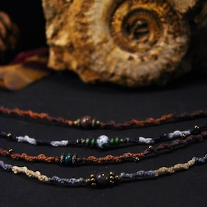 May include: Five braided cord bracelets with different coloured cords and beads. The bracelets feature brown, black, grey, and white cords with brown, green, and grey beads.