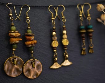 May include: Three pairs of dangle earrings with various beads and charms. The earrings feature a mix of brown, green, gold, and turquoise beads. The earrings are hanging on a dark background.