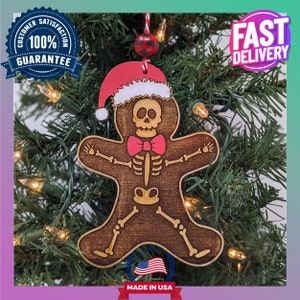 May include: A wooden gingerbread man Christmas ornament with a skeleton design, wearing a red and white Santa hat and a red bow tie. The ornament is hanging on a green Christmas tree.