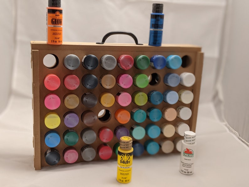 Puede incluir: Un organizador de pintura de madera con asa, que contiene una variedad de botellas de pintura de diferentes colores. El organizador tiene 48 ranuras para botellas de pintura. Las botellas de pintura son de 2 oz (59 ml).