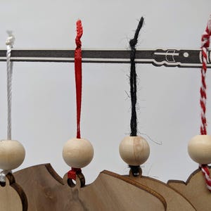 May include: Wooden ornaments with a lightsaber design, each suspended by a different colored string. The strings are white, red, black, and red-and-white striped. The ornaments are attached to a wooden base.