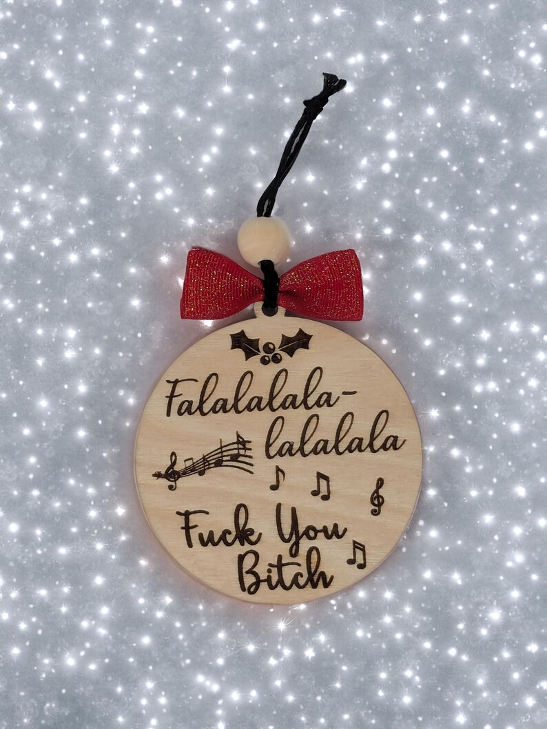 May include: Wooden Christmas ornament with the text "Falalalala-lalala Fuck You Bitch" and musical notes. The ornament has a red bow and a black string for hanging.