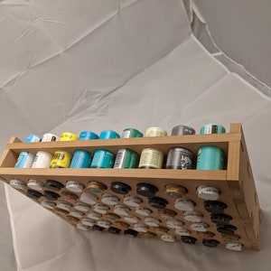Puede incluir: Un estante de almacenamiento de madera con dos estantes que sostienen filas de peque&ntilde;os contenedores redondos. Los contenedores est&aacute;n llenos de pintura de varios colores, incluyendo blanco, negro, verde, azul y amarillo.