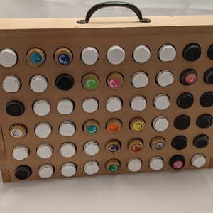 Puede incluir: Una caja de madera con una manija negra, que contiene una cuadr&iacute;cula de peque&ntilde;os frascos con tapas de colores. Los frascos est&aacute;n dispuestos en filas y columnas, y algunas de las tapas tienen dise&ntilde;os diferentes.