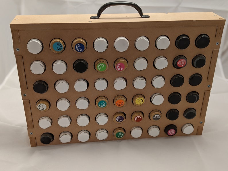 Puede incluir: Una caja de madera con una manija negra, que contiene una cuadr&iacute;cula de peque&ntilde;os frascos con tapas de colores. Los frascos est&aacute;n dispuestos en filas y columnas, y algunas de las tapas tienen dise&ntilde;os diferentes.