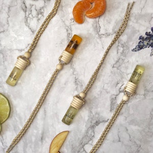 Puede incluir: Cuatro peque&ntilde;os frascos de vidrio con la palabra "adelia" impresa, suspendidos por cordones beige. Los frascos est&aacute;n dispuestos sobre una superficie de m&aacute;rmol, junto con rodajas de fruta y una ramita de lavanda. Los frascos tienen tapas y cuentas de madera.