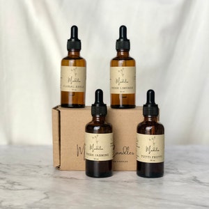 Puede incluir: Cuatro botellas de vidrio &aacute;mbar con cuentagotas negros, etiquetadas con aromas florales y frutales, incluyendo "Floral Apple" y "Tutti Frutti". Las botellas est&aacute;n dispuestas sobre una caja de cart&oacute;n marr&oacute;n, con la marca "Madelia Candles".