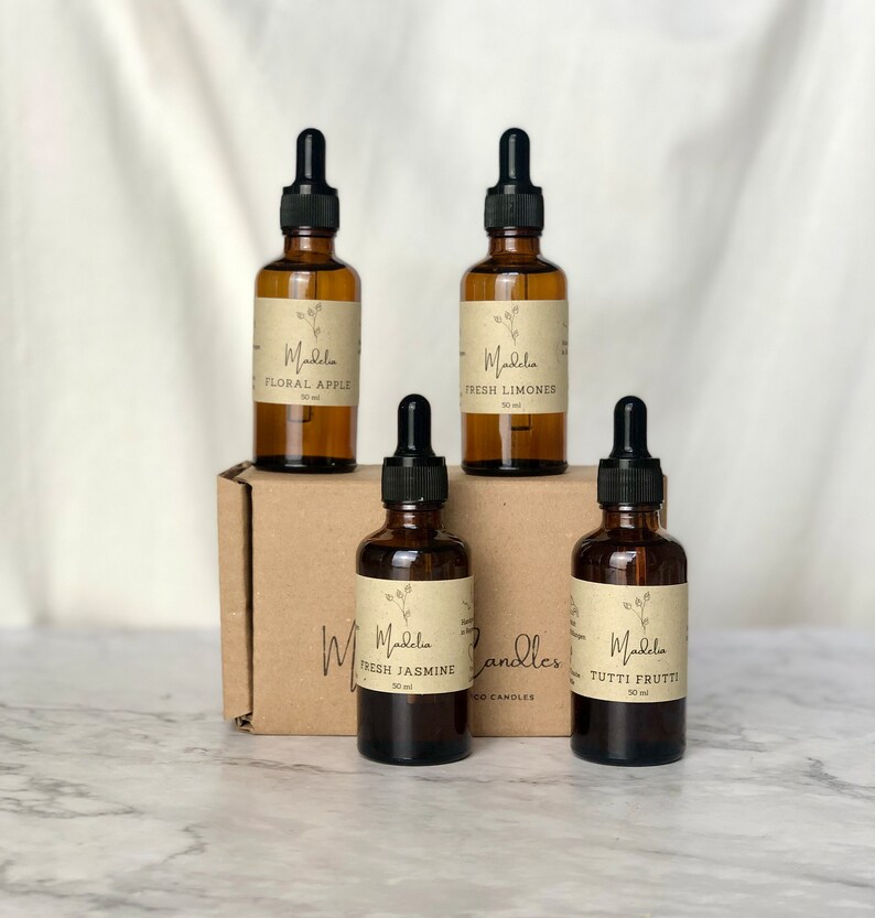 Puede incluir: Cuatro botellas de vidrio &aacute;mbar con cuentagotas negros, etiquetadas con aromas florales y frutales, incluyendo "Floral Apple" y "Tutti Frutti". Las botellas est&aacute;n dispuestas sobre una caja de cart&oacute;n marr&oacute;n, con la marca "Madelia Candles".