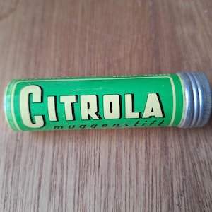 Op de afbeelding: Een groene en zilveren tube met de tekst "CITROLA muggenstift" erop gedrukt.