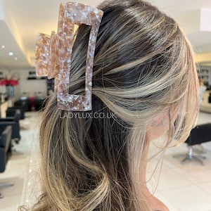 May include: A large, tortoiseshell-colored hair claw with a rectangular opening. The claw is made of a translucent material with a mottled pattern.