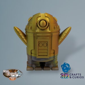 Puede incluir: Una figura de robot de color dorado con una cabeza redonda y dos brazos pequeños. El robot tiene una superficie texturizada y un brillo metálico. El robot está de pie sobre una superficie plana.