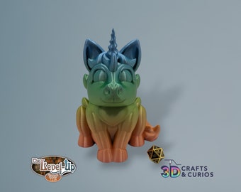 May include: A small, rainbow-colored unicorn figurine with a curled horn, sitting on a light blue background. The unicorn has a friendly expression and is made of 3D printed plastic.