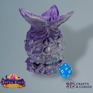 May include: Purple and silver 3D printed dice tower shaped like a monster with a blue dice on the bottom. The dice tower is labeled "Fates End Dice Towers & More"