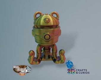 May include: A gold-colored, 3D printed robot with a dome-shaped head and multiple legs. The robot is standing on a white surface with a blue and white dice in the foreground. The text "3D CRAFTS & CURIOS" is visible in the lower right corner of the image.