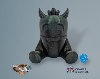 May include: A black 3D printed figurine of a small dragon with a collar. The dragon is sitting on a light blue surface with a blue 20-sided die in front of it. The die has white numbers on it. The image also includes a logo for "The Level-Up" and "3D Crafts & Curios".
