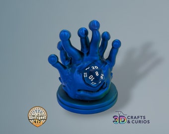 May include: A blue 3D printed dice holder shaped like a hand with multiple fingers. The holder is holding a blue 20-sided die with white numbers.