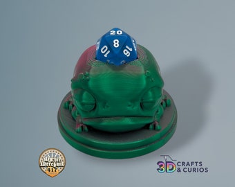 May include: A green and red 3D printed frog figurine with a blue 20-sided die on top. The die is showing a 19.