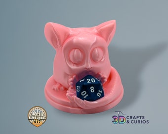 May include: A pink 3D printed figurine of a lemur holding a blue 20-sided die. The lemur is sitting on a pink base.