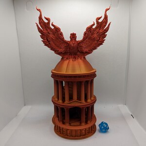 Puede incluir: Un modelo impreso en 3D de un fénix que surge de un templo circular. El fénix está hecho de filamento naranja y tiene las alas extendidas. El templo está hecho del mismo filamento naranja y tiene una serie de columnas y escalones.