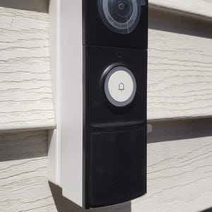May include: A white and black doorbell with a 180° ultra-wide view, a doorbell button, and a black rectangular area for a camera lens.