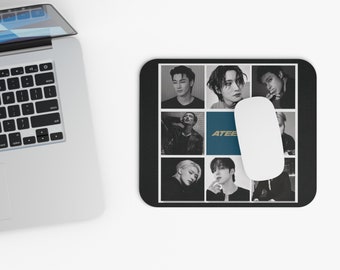 May include: Black mousepad featuring a grid of black and white portraits of people. The word "ATEEZ" is printed in blue on the mousepad. A white computer mouse rests on the mousepad, next to a laptop.