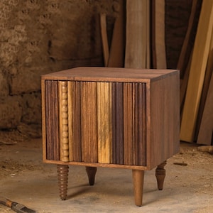 Pu&ograve; includere: Un comodino in legno fatto a mano con un design frontale unico con doghe di legno verticali in varie tonalit&agrave; di marrone e beige. Il comodino ha quattro gambe, con le due gambe anteriori con un design a spirale. Lo stile generale &egrave; rustico e moderno.