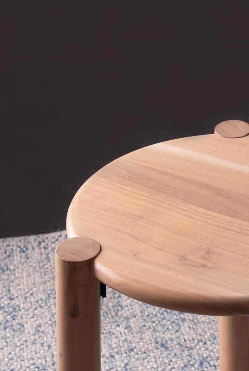 May include: A round wooden stool featuring a smooth, light-toned circular top and three thick, cylindrical legs that connect to the surface with visible circular joints. The natural wood grain is clearly visible across the entire structure.