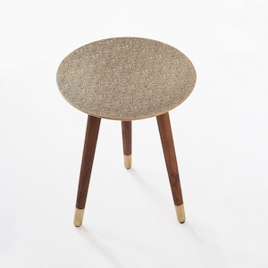 Peut inclure: Petite table d'appoint ronde avec un plateau doré à motifs et trois pieds en bois brun foncé. Les pieds ont des embouts dorés. La table est une pièce décorative.