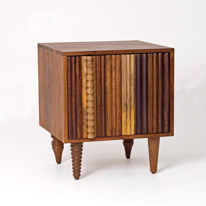 Pu&ograve; includere: Un comodino in legno con un fronte a coste verticali multicolore. Il comodino ha un piano quadrato ed &egrave; sostenuto da quattro gambe corte e tornite. Le tonalit&agrave; del legno variano dal marrone chiaro allo scuro.