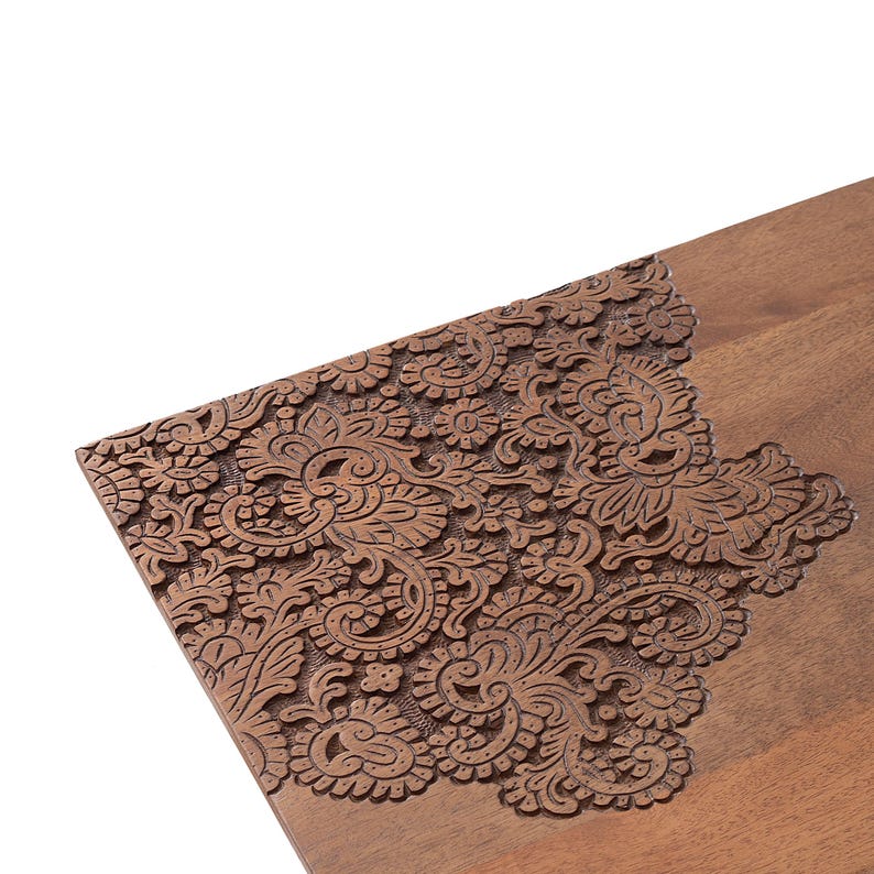K&ouml;nnte beinhalten: Nahaufnahme einer Holzoberfl&auml;che mit aufwendigen Blumenschnitzereien. Das detaillierte Design zeigt wirbelnde Muster und botanische Elemente und bildet einen strukturierten, dekorativen Rand an der Ecke des Holzst&uuml;cks.