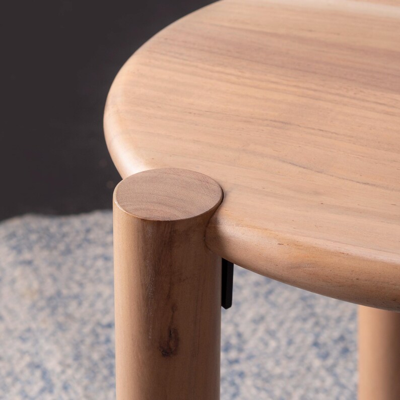May include: A light-colored wooden side table with a round top and cylindrical legs. The table has a natural wood grain finish and a minimalist design. The table is suitable for a living room or bedroom.