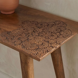 K&ouml;nnte beinhalten: Eine braune Holzkonsolentisch mit einem geschnitzten Blumendesign auf der Oberseite. Der Tisch hat eine rechteckige Oberseite und vier abgewinkelte Beine. Das geschnitzte Design bedeckt die vordere linke Ecke des Tisches.