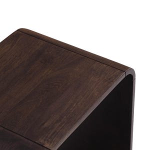 Op de afbeelding: Een donkerbruine houten bijzettafel met een gebogen ontwerp. De tafel heeft een glad, gepolijst oppervlak en een moderne uitstraling. De houtnerf is zichtbaar en voegt textuur toe aan het stuk.